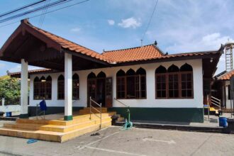 Front view of a white building with orange tiled roof, arched windows, and a yellow-tiled entrance stairs leading to a porch.