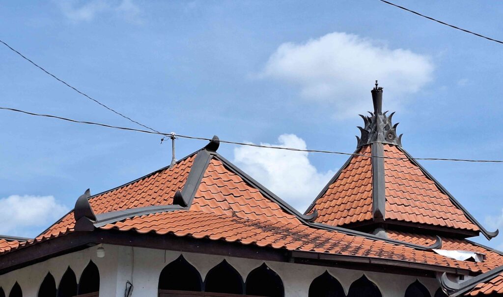 20260508_113516 - Mabur.co Temple-style roof with red clay tiles and a tall decorative finial against a blue sky, with power lines crossing the scene.