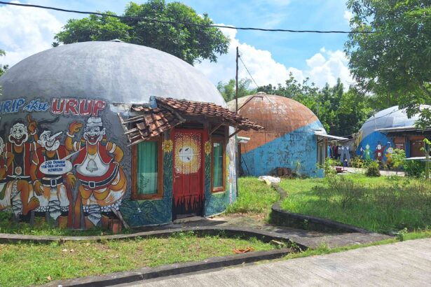 Colorful dome-shaped buildings with large cartoon mural outside, red doors, and a tiled roof, set in a sunny tropical yard.