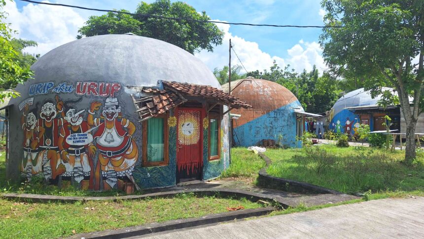 20260525_112539 - Mabur.co Colorful dome-shaped buildings with large cartoon mural outside, red doors, and a tiled roof, set in a sunny tropical yard.
