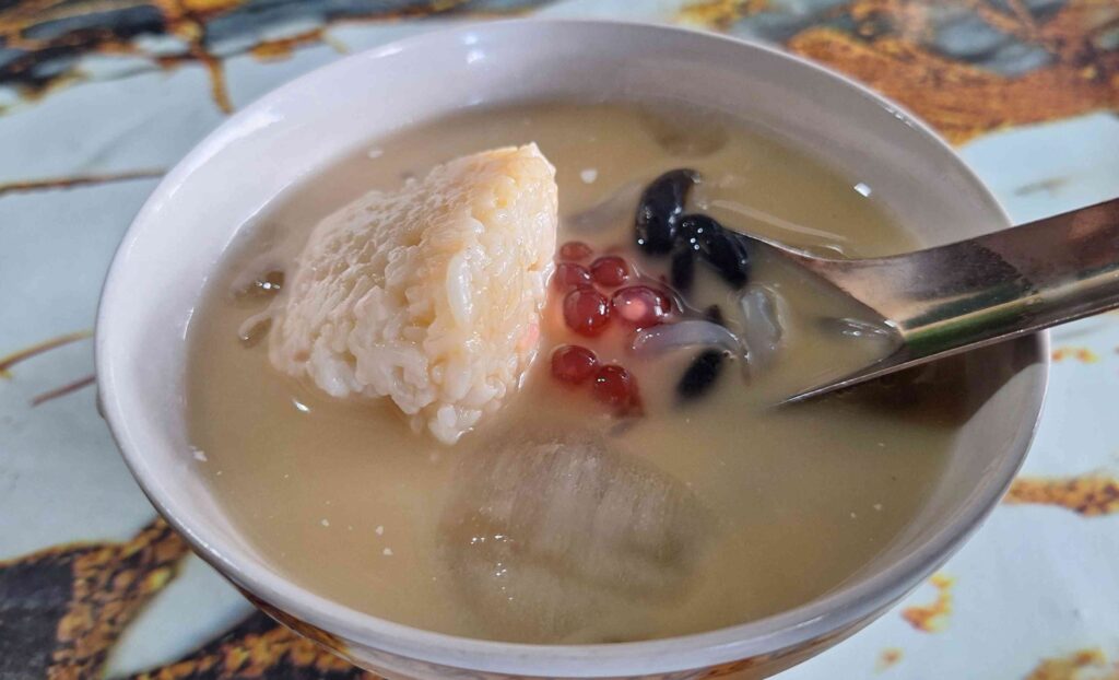 Creamy coconut milk dessert with sticky rice, red beans, and black beans in a white bowl with a spoon nearby.