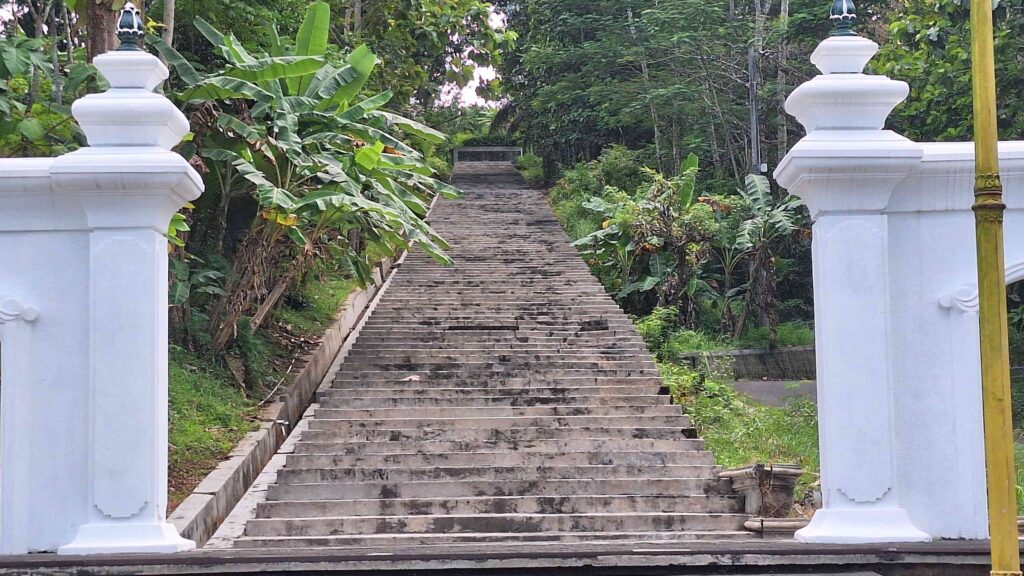 20260603_120142 - Mabur.co Stone staircase leading up through a lush tropical garden, framed by white decorative gateposts on either side.