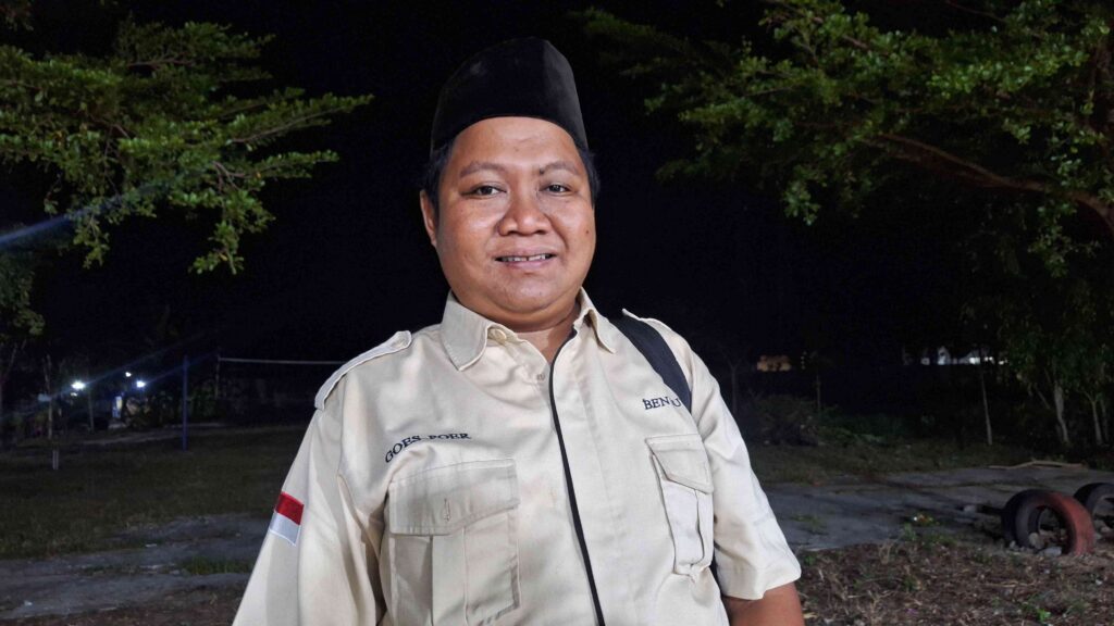 20260615_213032 - Mabur.co Man in a light khaki uniform and black hat outdoors at night, smiling with trees in the background.