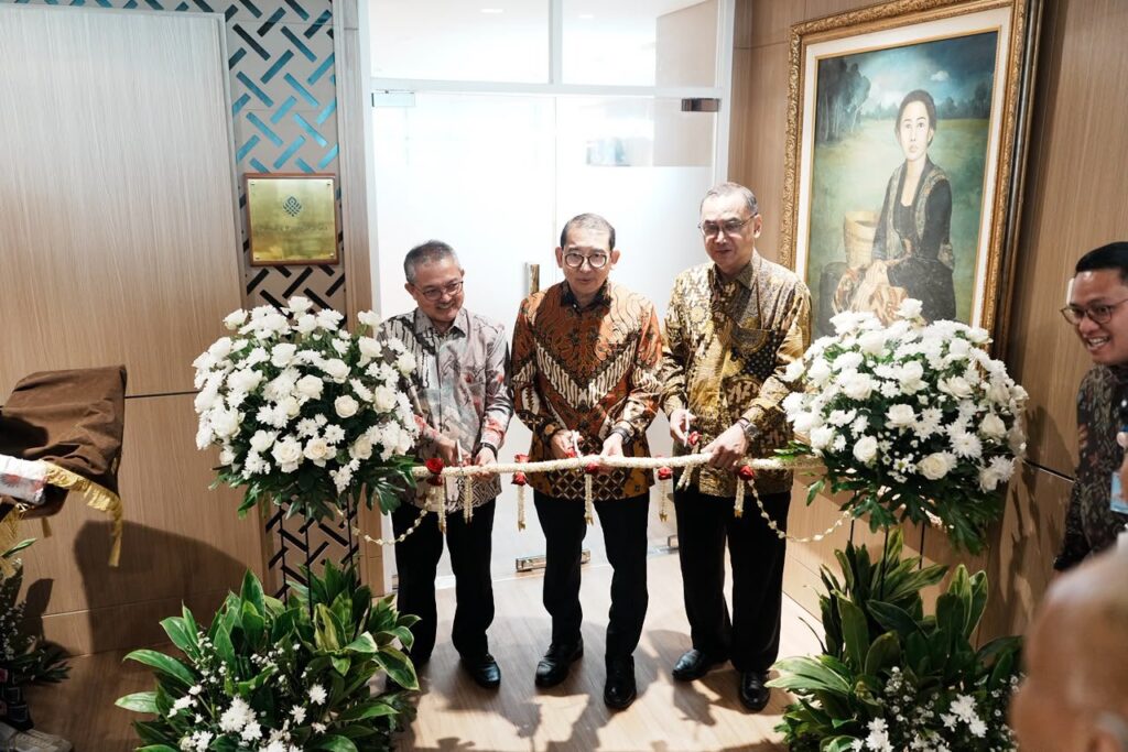 20260720_225706 - Mabur.co Four men in batik shirts cut a white floral ribbon during a ceremonial opening, flanked by two large flower arrangements in a modern lobby.