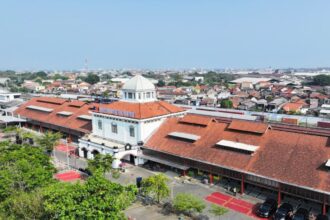 Aerial view of a railway station complex with red-tiled roofs and a white-domed central building, in a small town.