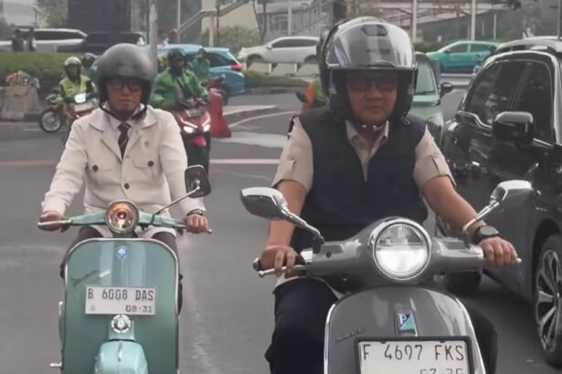 Two scooter riders in traffic: a man wearing a helmet and vest on a gray scooter in the foreground, and a woman in a beige jacket on a mint-green scooter behind him.