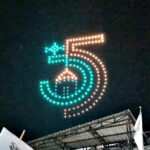 Night scene of a large LED-dot sign forming the number five in teal and orange above a stage at night.