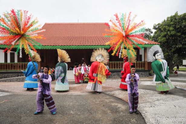 Group of performers in colorful traditional costumes with large masks dancing in an open courtyard under festive paper palm decorations above.