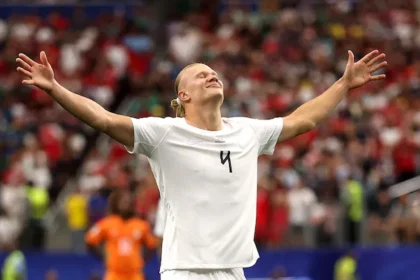 Soccer player in a white jersey with arms raised in celebration on a filled stadium field.