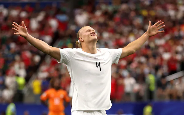 Soccer player in a white jersey with arms raised in celebration on a filled stadium field.