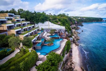 A terraced seaside resort with multiple blue pools, white buildings, and lush greenery along a rocky coastline.