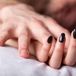 Close-up of a hand with black nail polish resting on white bedsheet, fingers relaxed on a pillow-like surface thinking image of a person lying down.