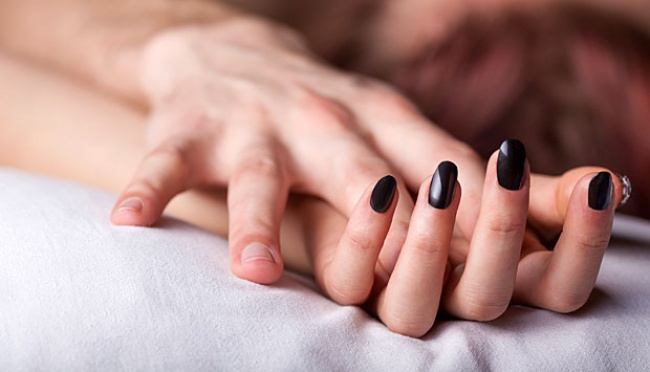 Close-up of a hand with black nail polish resting on white bedsheet, fingers relaxed on a pillow-like surface thinking image of a person lying down.