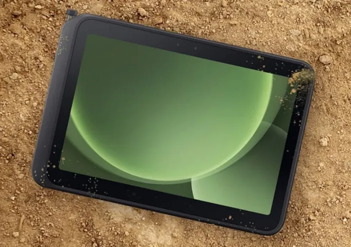 Rugged tablet lying on dirt ground, screen showing green abstract circular graphics.