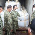 Indonesian soldiers in camouflage and masks inspect large white-wrapped cargo secured inside a shipping container.