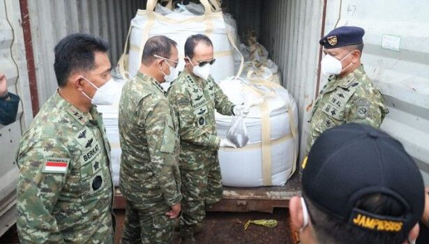 Indonesian soldiers in camouflage and masks inspect large white-wrapped cargo secured inside a shipping container.