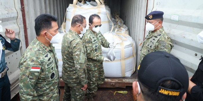 Indonesian soldiers in camouflage and masks inspect large white-wrapped cargo secured inside a shipping container.
