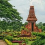 Red brick, pagoda-like temple in a manicured garden with pathways and trees surrounding it.