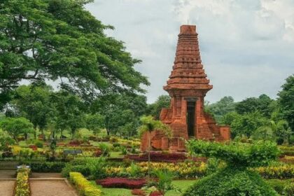 Red brick, pagoda-like temple in a manicured garden with pathways and trees surrounding it.