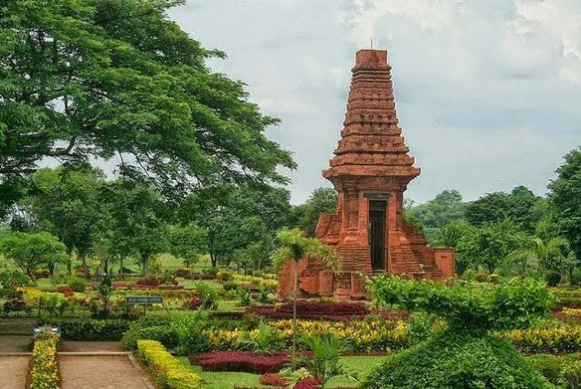 Red brick, pagoda-like temple in a manicured garden with pathways and trees surrounding it.
