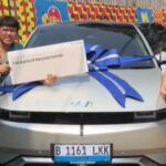 Two people pose beside a silver car with a large blue ribbon; the person on the left holds a sign reading 'I'm a proud Hyundai family'.