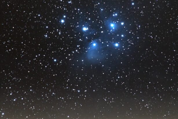 Star-filled night sky over a lit town on rolling hills, with a blue-trim cluster of stars near the top center.