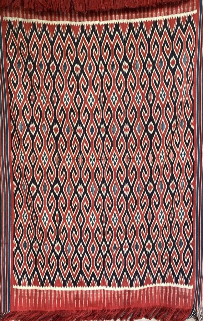 482756296_18399776650101682_840936493298072166_n - Mabur.co Diamond- and chevron-pattern rug in red, navy, and white with fringe along top and bottom edges, hanging as a wall weave or decorative textile at the sides requested by context.