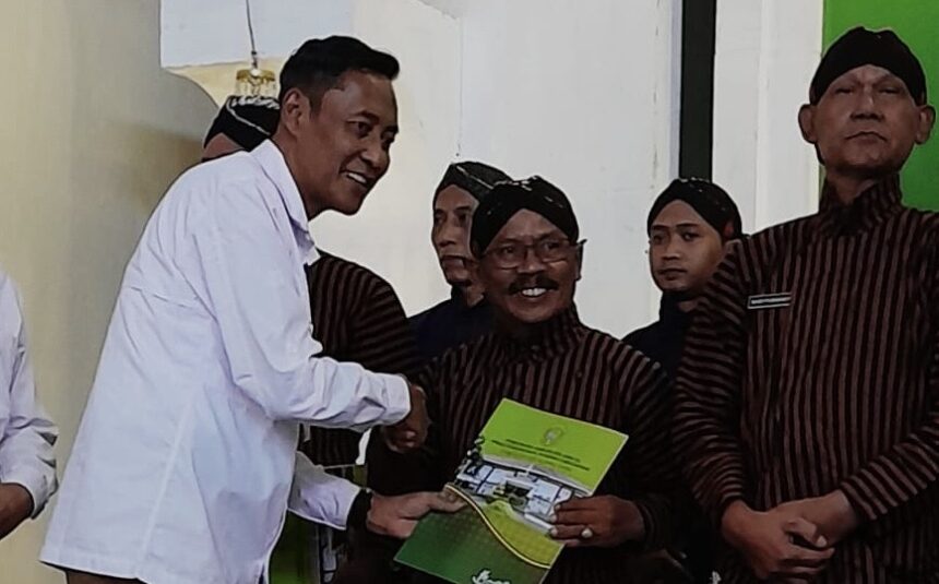 Man in a white shirt shakes hands with a smiling recipient in a brown striped uniform while presenting a green certificate.