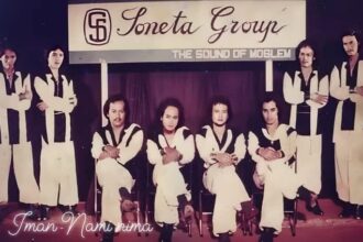 Nine-member band posing on a stage in matching white outfits with black trim; banner above reads 'Soneta Group' and subtitle 'The Sound of ...' as they sit and stand in a row.