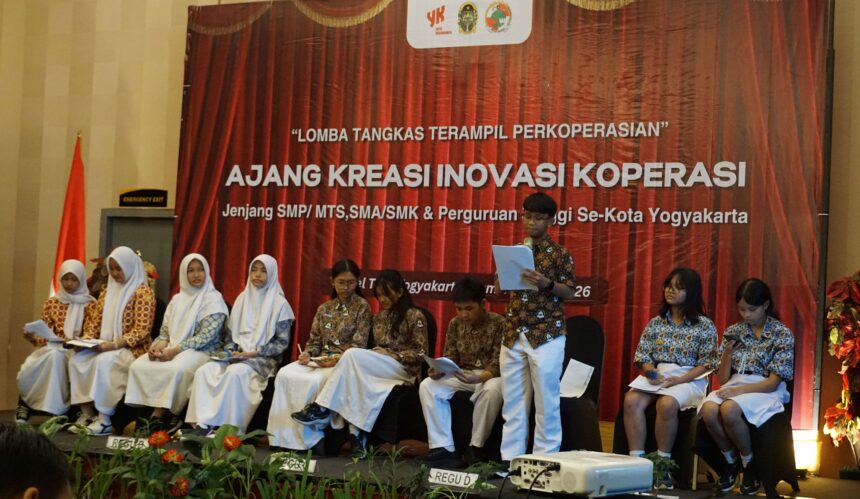 567 - Mabur.co Students in batik and white hijabs sit on a stage during a cooperative creativity event; red backdrop reads 'AJANG KREASI INOVASI KOPERASI' with logos above.