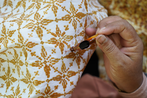 Close-up of a hand holding a small needle near brown embroidered floral pattern on white fabric, illustrating sewing detail