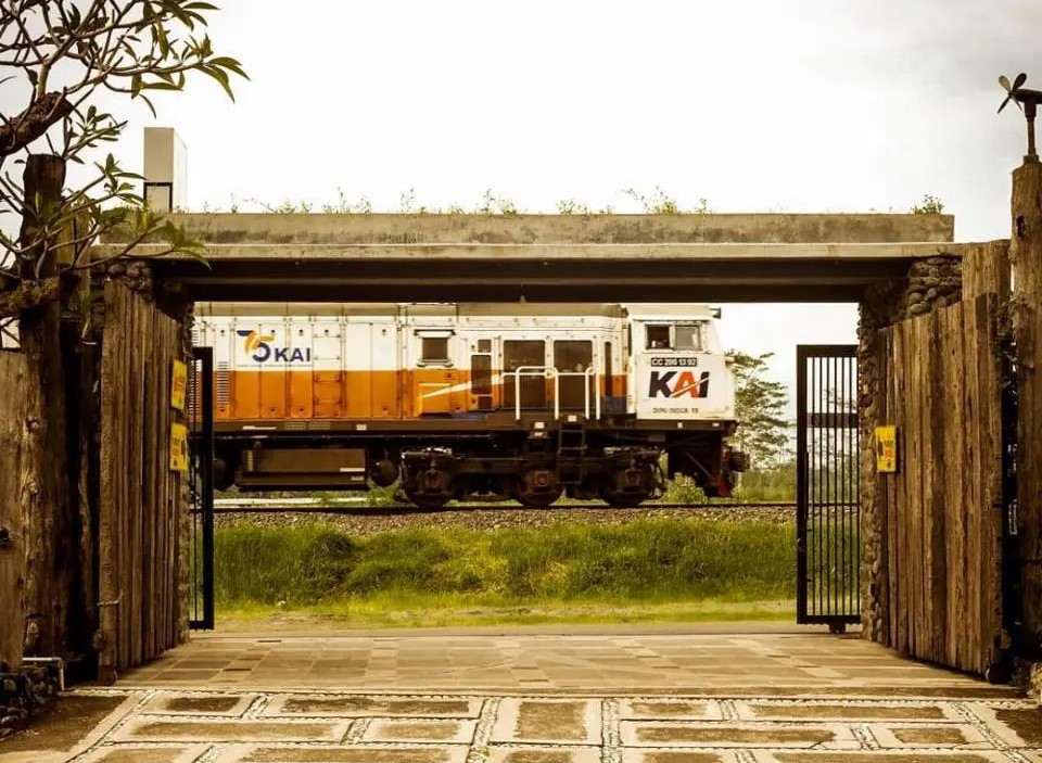 Locomotive on train tracks seen through an open stone gate with greenery beyond the rails.
