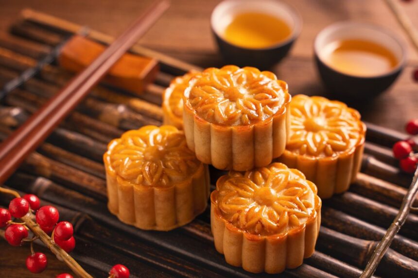 Mooncakes with flower-patterned tops stacked on a wooden surface with tea cups in the background.