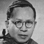 Black-and-white portrait of a man with round glasses looking at the camera.