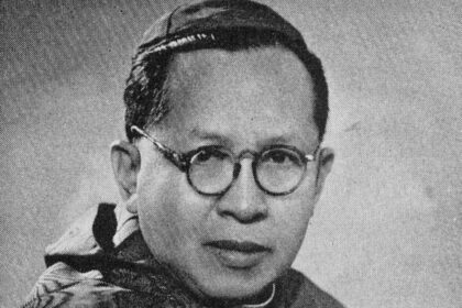 Black-and-white portrait of a man with round glasses looking at the camera.