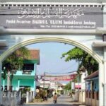 Gateway arch of Pondok Pesantren Bahrl Ulum Tambakberas Jombang, opening onto a residential street with a motorbike in view beyond the arch.