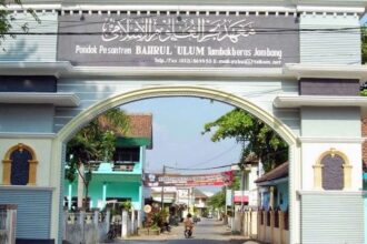 Gateway arch of Pondok Pesantren Bahrl Ulum Tambakberas Jombang, opening onto a residential street with a motorbike in view beyond the arch.