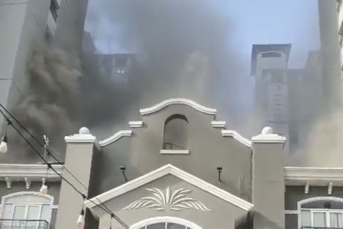 Gray ornate building in the foreground with thick black smoke rising from behind it, indicating a fire in the background.