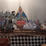 Colorful cutout puppets arranged on a stage, depicting a mythological scene with deities and warriors, with rods in front for manipulation.