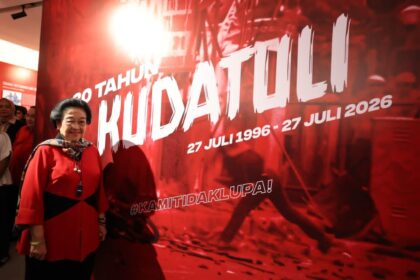 Smiling woman in a red outfit posing beside a large red banner with white text and dates.