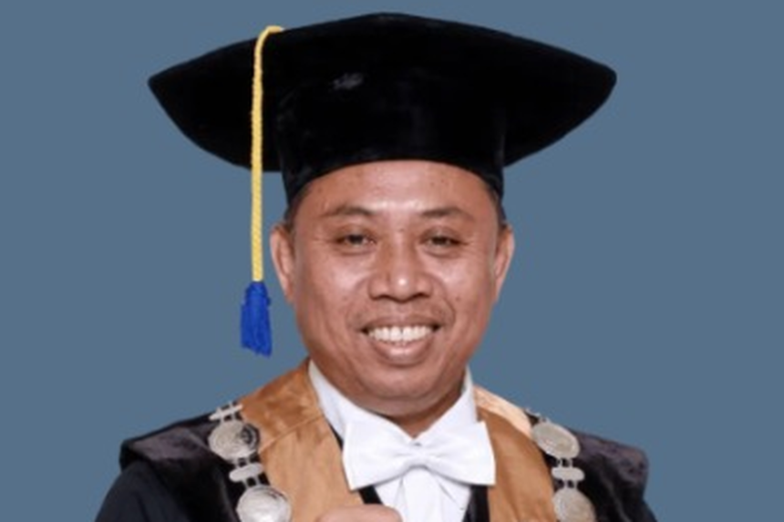 Smiling man in graduation gown and cap with blue tassel against a blue background, ready for a ceremony