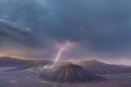 Volcanic crater landscape under stormy clouds with a bright lightning bolt striking the crater area at dusk.