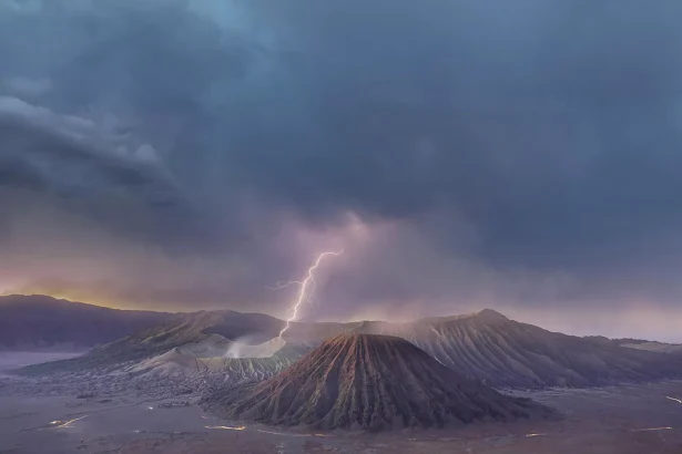 Volcanic crater landscape under stormy clouds with a bright lightning bolt striking the crater area at dusk.