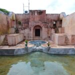 Pink stucco fort courtyard with staircases on both sides, arches, and a central circular fountain surrounded by a shallow pool.