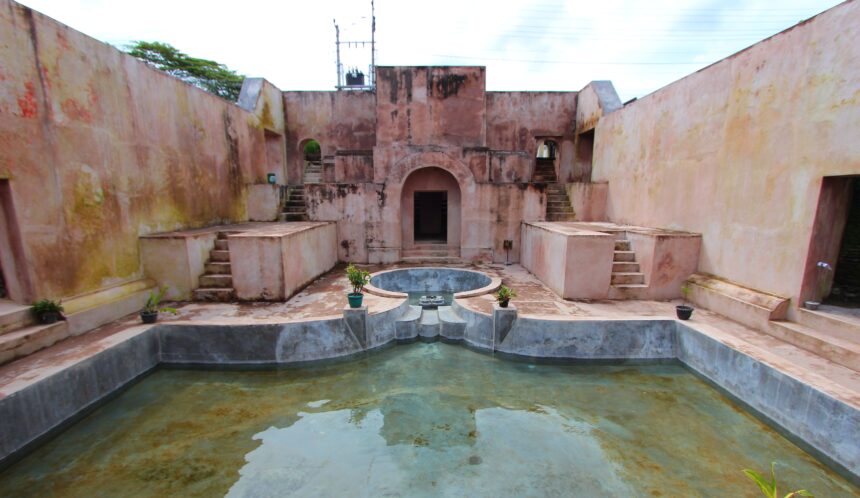 70d3da44ebfac2cf109af48b4d7e0594 - Mabur.co Pink stucco fort courtyard with staircases on both sides, arches, and a central circular fountain surrounded by a shallow pool.