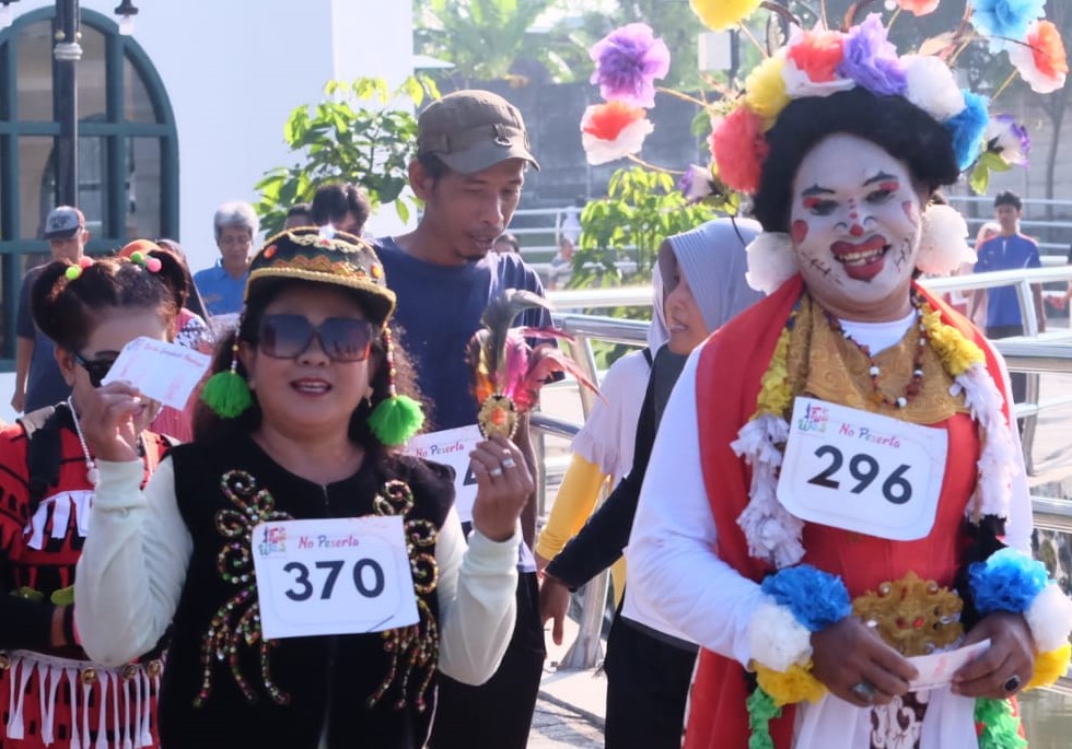 Clown in colorful costume and flower headdress beside parade participants wearing bibs 370 and 296.