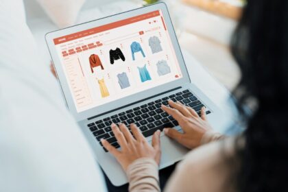 Person typing on a laptop browsing an online clothing store with a grid of dresses and shirts.