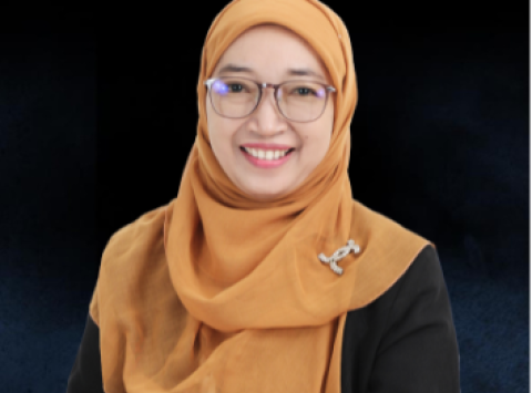 Portrait of a smiling woman wearing an orange hijab, glasses, and a black blazer with a decorative pin against a dark background.