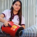 Young woman in a polo shirt operates a red portable fire-safety device aimed at flames during a demonstration.