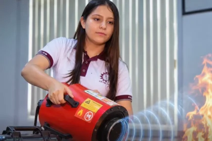 Young woman in a polo shirt operates a red portable fire-safety device aimed at flames during a demonstration.